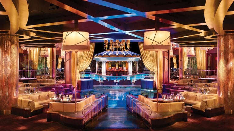 Luxury nightclub interior with symmetrical layout, blue and purple lighting, cream colored seating, illuminated bar, and geometric ceiling design