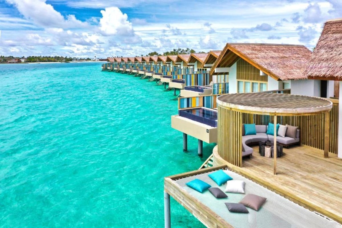 Tropical overwater bungalows with thatched roofs and wooden decks lined along turquoise lagoon water under blue sky