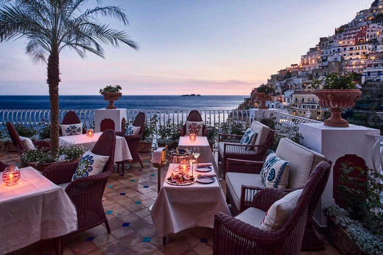 Elegant seaside dining terrace at dusk with candlelit tables overlooking the Mediterranean coastline and cliffside town